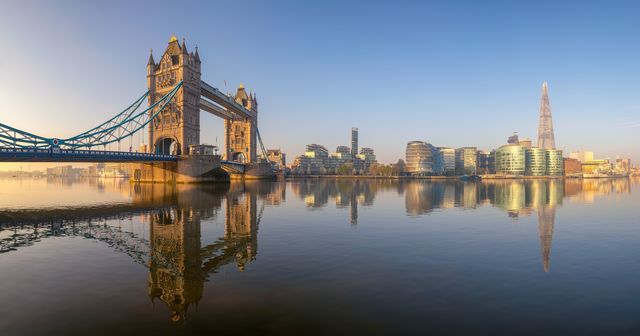 A panoramic view of the River Thames, spanning from Tower Bridge to the Shard. The still water offers a perfect reflection of the city skyline.