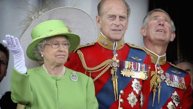 Queen Elizabeth II raises her hand during a downpour as she stands with (L-R) Prince Philip, Duke of Edinburgh and Prince Charles, Prince of Wales on the balcony of Buckingham Palace after the Trooping the Colour ceremony on June 16, 2007 in London. Each year the official birthday of Queen Elizabeth II is commemorated with a military parade and march-past of fully trained, operational troops from the Household Division