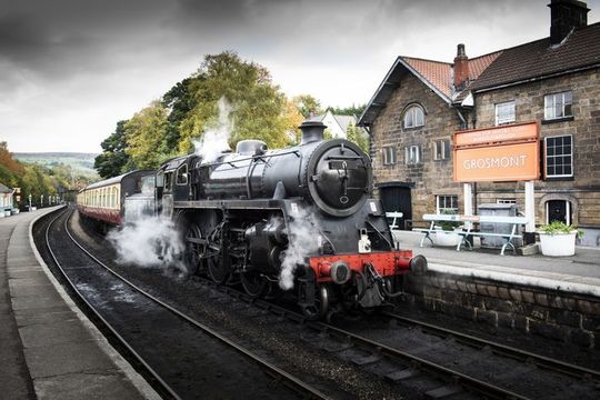 A stream train arriving at the platform of a traditional station in North Yorkshire.