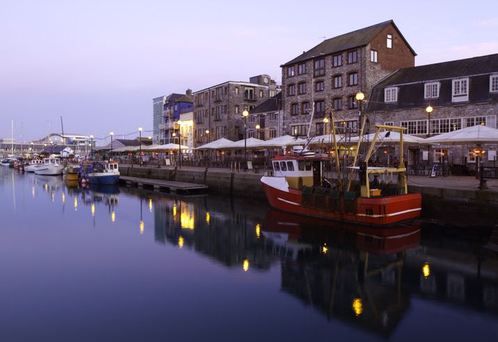 A tranquil scene at Plymouth Barbican, a historic part of Plymouth which is a popular location for tourists and residence.The photos shows the calm waters of the harbour with bars and restaurants in the background.