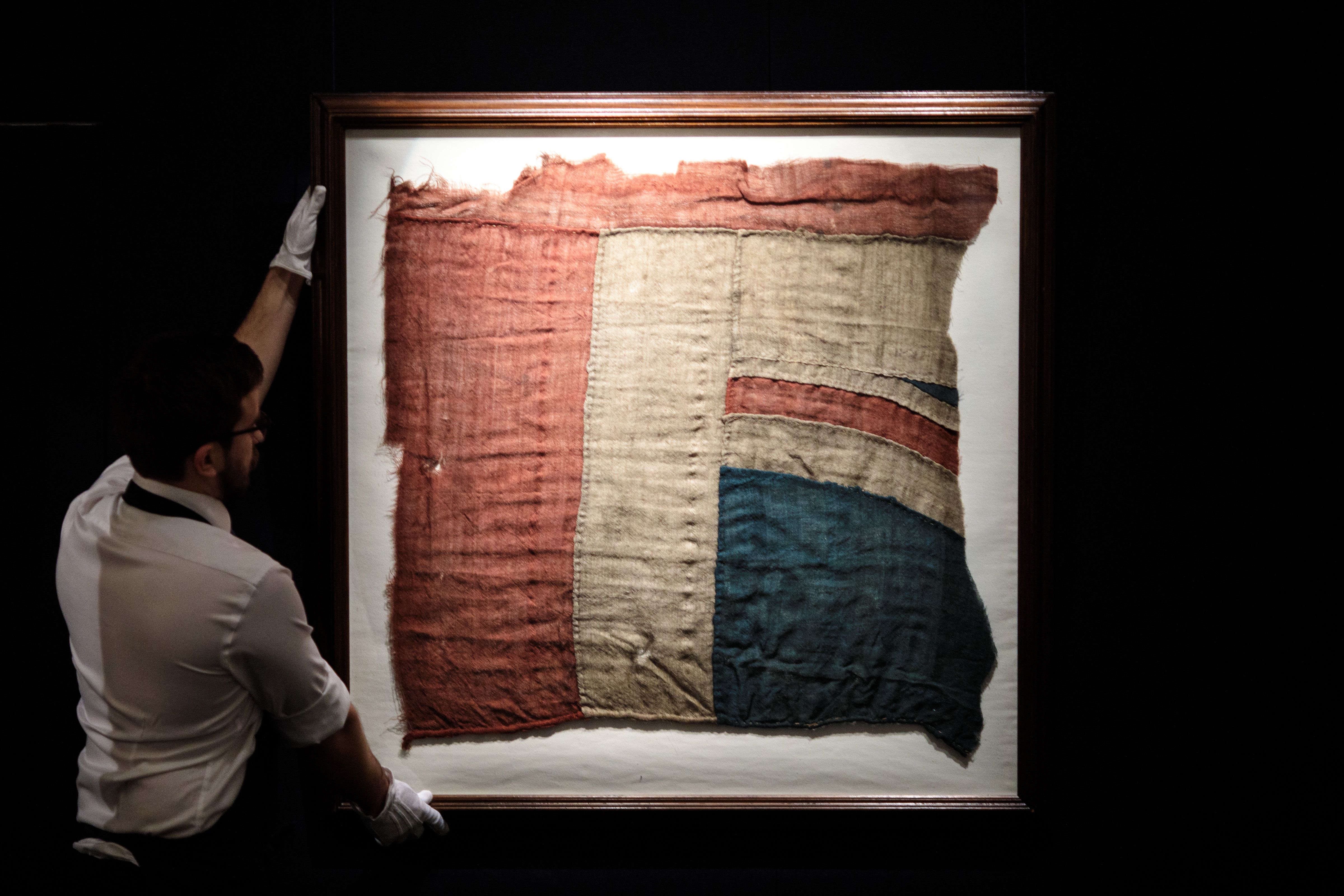 Un employé pose avec un grand fragment du drapeau Union Jack qui aurait flotté sur le navire de Lord Horatio Nelson, le HMS Victory lors de la bataille de Trafalgar (est. 80 000 - 100 000 £) chez Sotheby's le 11 janvier 2018 à Londres, en Angleterre.'s ship, the HMS Victory at the battle of Trafalgar (est. £80,000 - 100,000) at Sotheby's on January 11, 2018 in London, England.