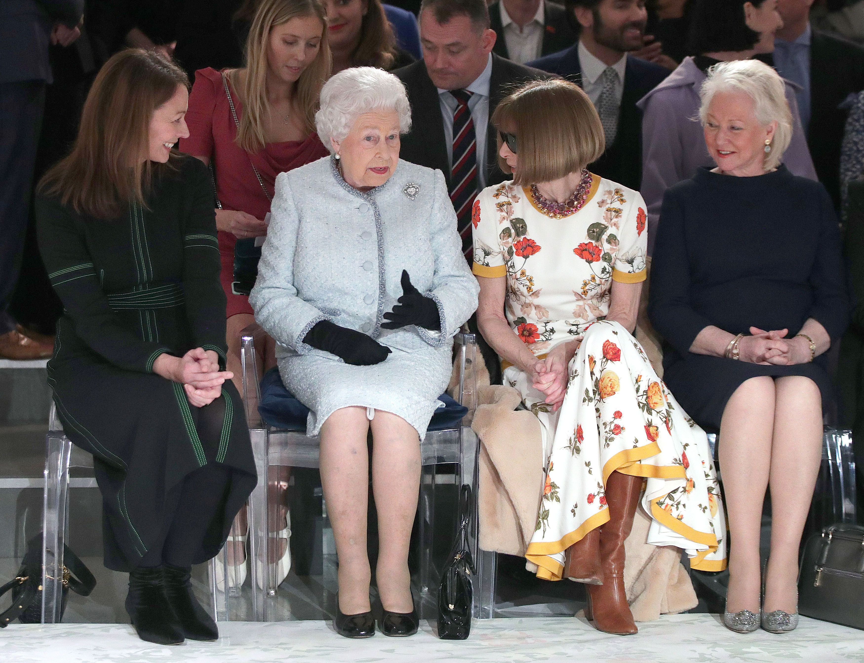 Elizabeth II sits with Anna Wintour, Caroline Rush (L), chief executive of the British Fashion Council (BFC) and royal dressmaker Angela Kelly (R) as they view Richard Quinn's runway show before presenting him with the inaugural Queen Elizabeth II Award for British Design as she visits London Fashion Week's BFC Show Space on February 20, 2018 in London, United Kingdom. (Photo by Yui Mok - Pool/Getty Images)